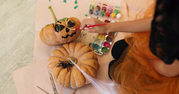 Little girl drawing face on orange Halloween pumpkin