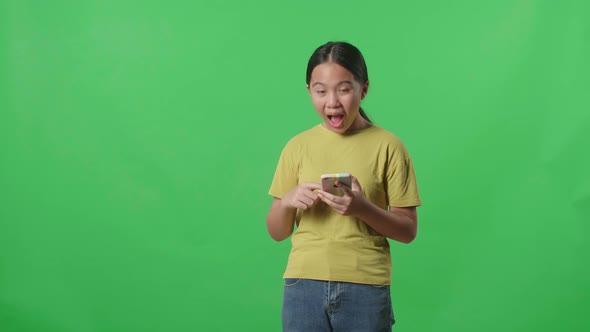 Smiling Kid Girl Use Mobile Phone And Pointing To Smart Phone Screen In Green Screen Studio