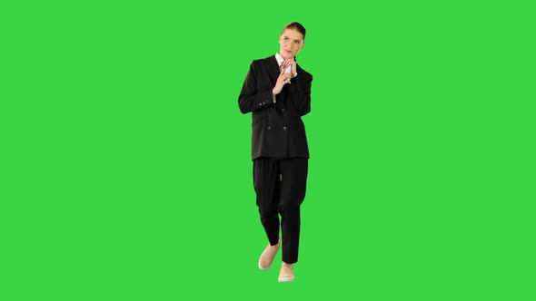 Young Woman in Office Suit Walking Typing Some Text on Her Smartphone and Smiling on a Green Screen