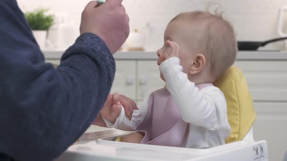 Father Feeding His Baby in the Kitchen at Home Closeup of Oneyearold Baby Boy in White High Baby