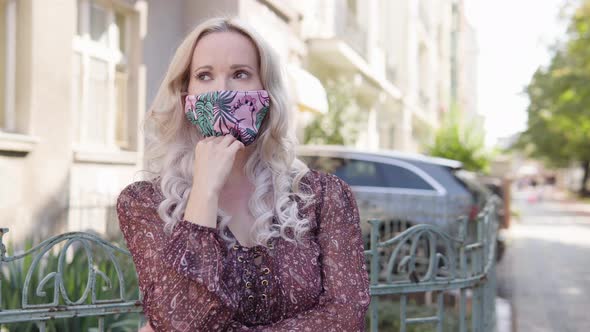 A Middleaged Caucasian Woman in a Face Mask Thinks About Something in an Urban Area