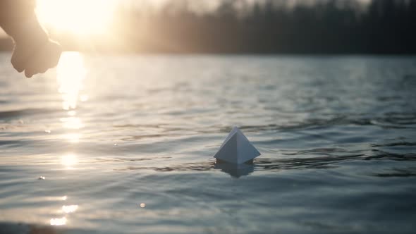 Paper Boat On River At Sunset. Origami Ship Sailing On Pond. Man Hand Launch Paper Boat On Water.