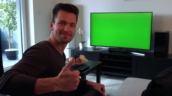 A Man Watches a TV with a Green Screen, Then Turns To the Camera, Smiles and Shows a Thumb Up