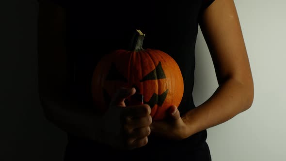 A woman holds a pumpkin in her hands for the Halloween holiday and makes a backlight