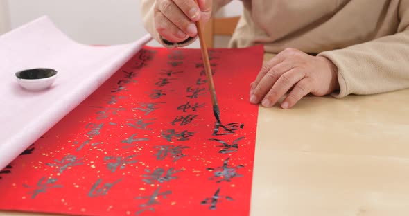 Asian man writing chinese calligraphy on red paper