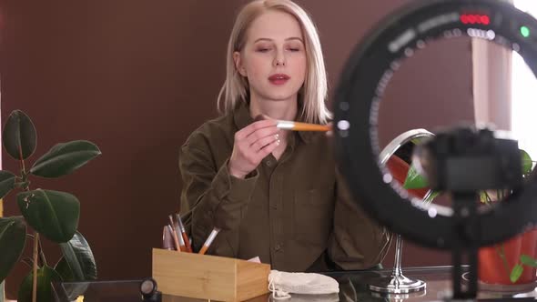 Beautiful blond hair woman applying makeup on camera for a vlog at home