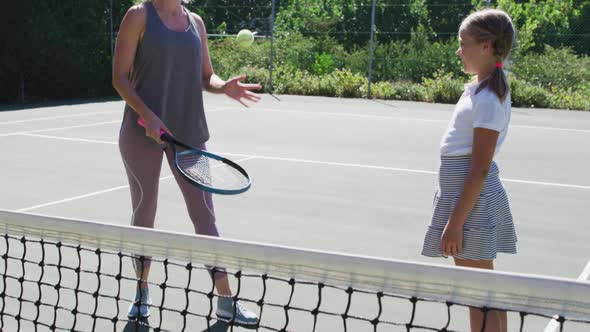 Caucasian mother teaching her daughter to play tennis at tennis court on a bright sunny day