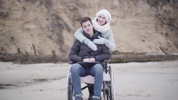 Portrait of Smiling Caucasian Woman Hugging Disabled Man in Wheelchair. Young Handicapped Boy and