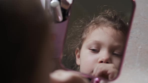 Little Girl at Home Sitting in Front of a Mirror and Painting Her Lips with Lipstick