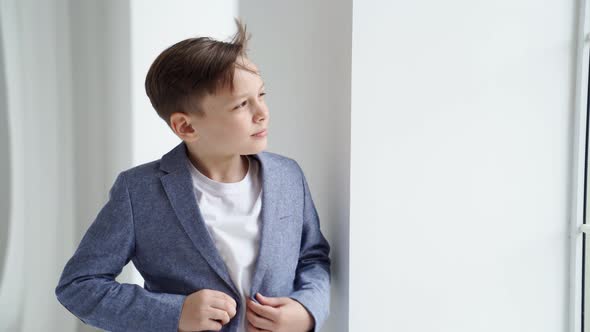 A Teenage Boy in a Jacket and Jeans Poses Standing By a Window