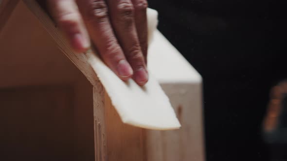 Unidentifiable Man is Sanding the Edges of a Wooden Birdhouse with Sandpaper