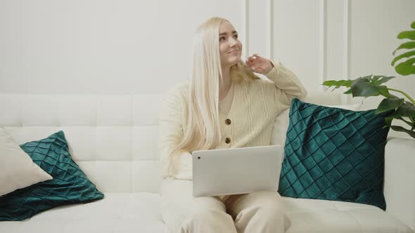 Caucasian Young Blonde Businesswoman Shopping Online Via Her Laptop Sitting on a Sofa in Her Modern