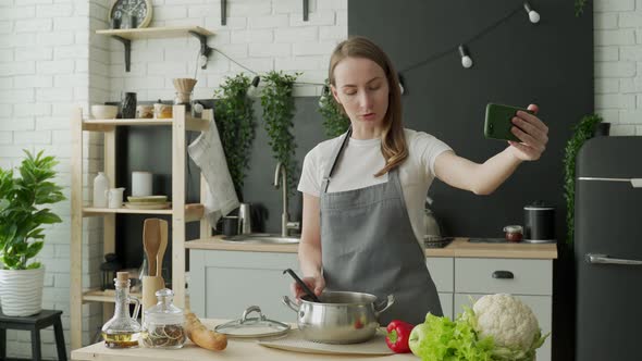 Happy Positive Female Blogger in an Apron Records a Cooking Video Blog on Her Mobile Phone