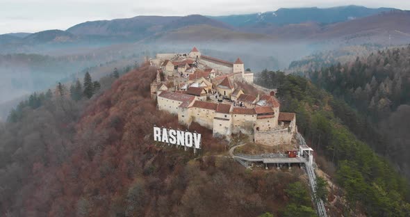 Aerial, orbit, drone shot, around the Rasnov citadel, on a foggy, overcast, fall day, in Transylvani