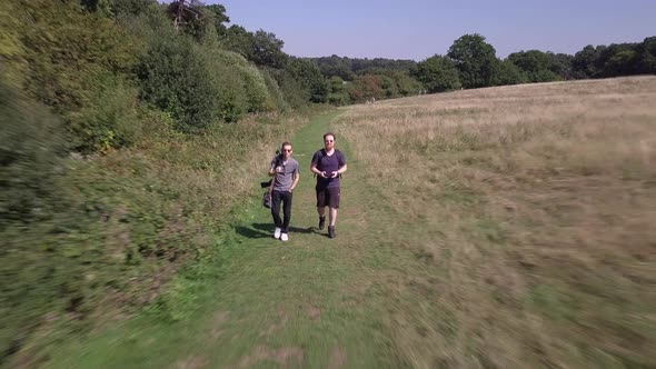 Drone flying away from 2 guys walking in woods in Trent Park North London UK. Sunny day time.