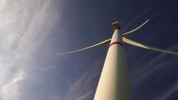 Blades of a Large Wind Turbine in a Field Against a Background of Cloudy Blue Sky on the Horizon
