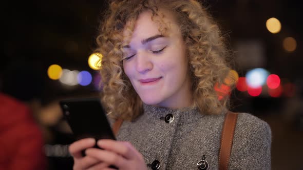 Woman Is Chatting in the Smartphone Against the Background of the Evening City