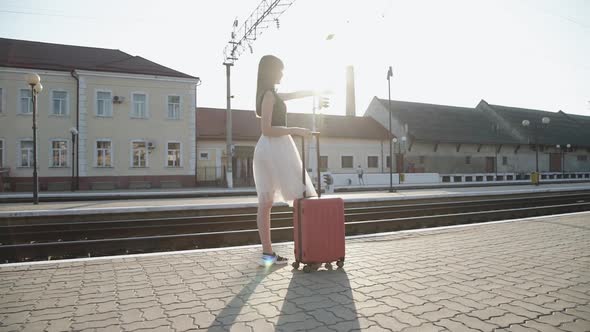 Elegant Lady Stands with Suitcase on Platform and Reach Hand Out To Distance