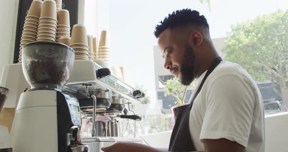 Happy african american male barista making coffee using coffe machine at cafe