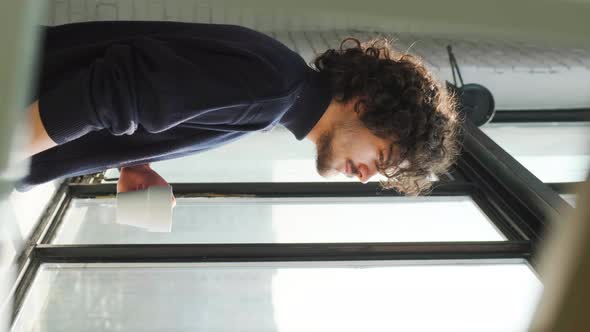 Man with Curly Hair Looking Out of Window Thinking Drinking a Cup of Tea or Coffee