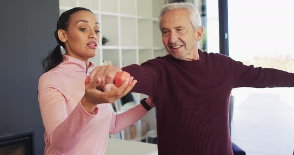 Video of happy biracial female physiotherapist exercising with caucasian senior man