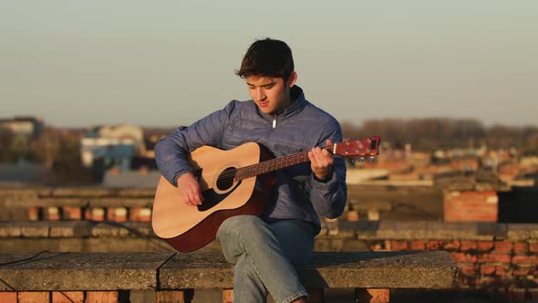 Young Guy in the Sunset Plays Guitar on the Roof of the House. Freedom Concept