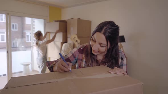 Closeup Portrait of a Young Woman Writing on Cardboard Boxes Labeling Them for Moving