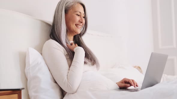 Positive Asian woman talking by video call on laptop