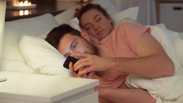 Man Using Smartphone While Girlfriend Is Sleeping 