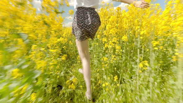 Woman Runs Quickly Through Meadow of Flowering Rapeseed Smiling Her Arms Open