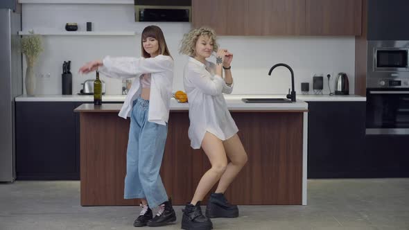 Wide Shot Dance of Two Happy Slim Beautiful Caucasian Women in Kitchen at Home