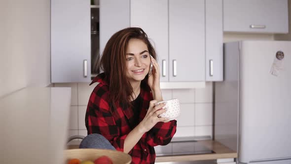 Young Beautiful Girl Starts Calling Someone While Sitting in Her Kitchen and Having a Cup of Tea in