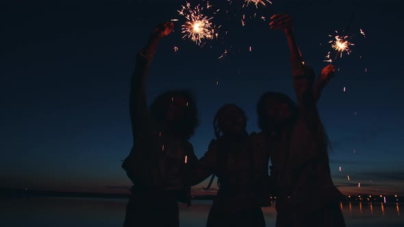 Portrait of Happy Female Friends Standing Outdoors on Beach Waving Sparklers and Enjoying Night