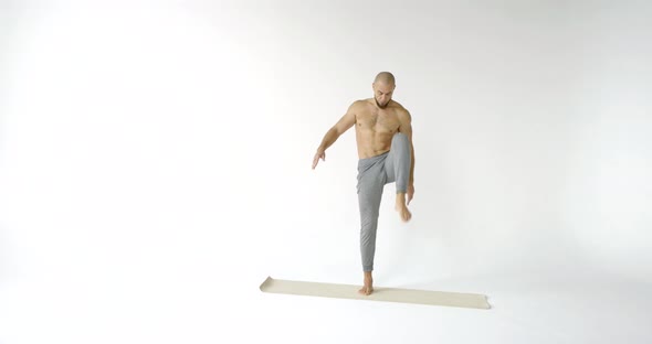 A Flexible and Plastic Male Yogi with a Beard Does Yoga on a Rug in a White Studio