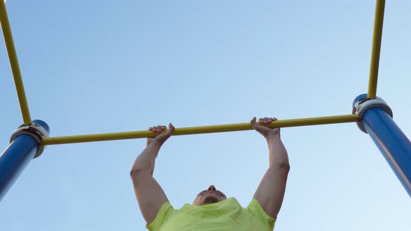 Caucasian Man Pulls Himself Up on Street Sports Field on Warm Summer Morning