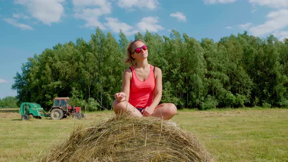 Beautiful Girl on a Sunny Day in Red Tshirt and Glasses Sits on Haystack Smiles