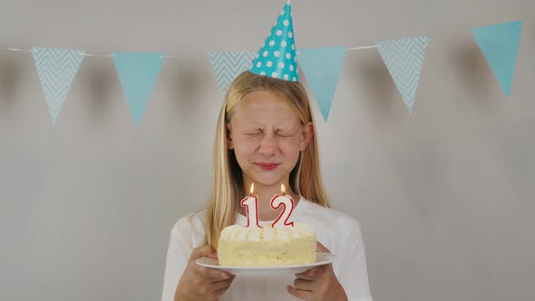 Cute Girl with Closed Eyes Making a Wish and Blowing Out the Candles Number Twelve on a Birthday