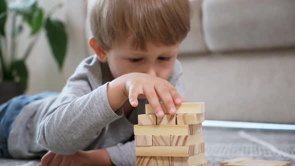 Child Builds a Wooden Tower for Playing with Wooden Blocks Lying on the Floor at Home