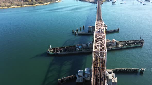 An aerial shot over elevated train tracks crossing a bay in Queens, NY. The camera dolly directly ov