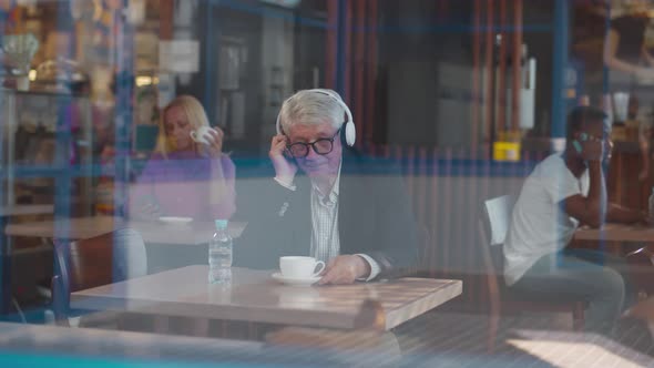 Senior Businessman in Headphones Drink Coffee in Restaurant