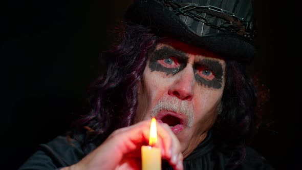 Frightening Creepy Senior Man with Halloween Witcher Makeup Looking at Candle Conjure Hex Wiz