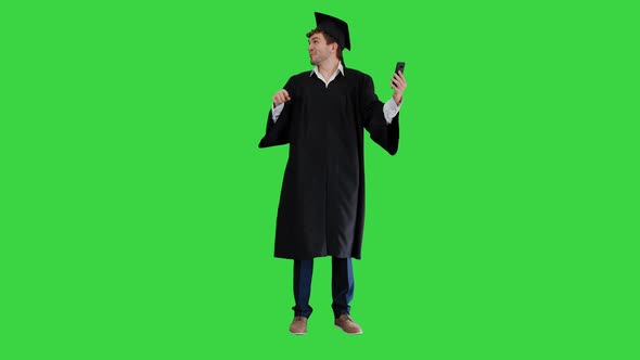 Happy Male Graduate in Gown and Mortarboard Having Emotional Video Call on His Phone on a Green