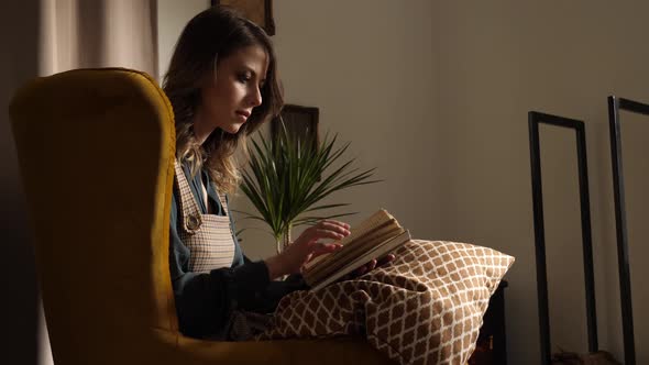 Woman sits in armchair and read a book at home