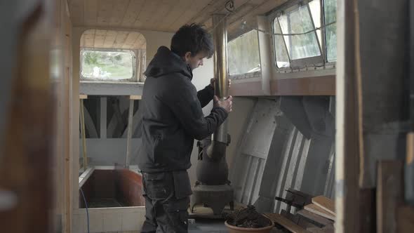 Young man fitting chimney pipe for wood burning stove interior wooden boat