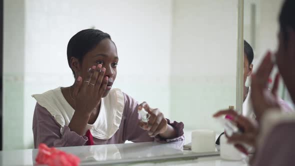 Reflection of Young Slim African American Woman Applying Face Moisturizer in Slow Motion