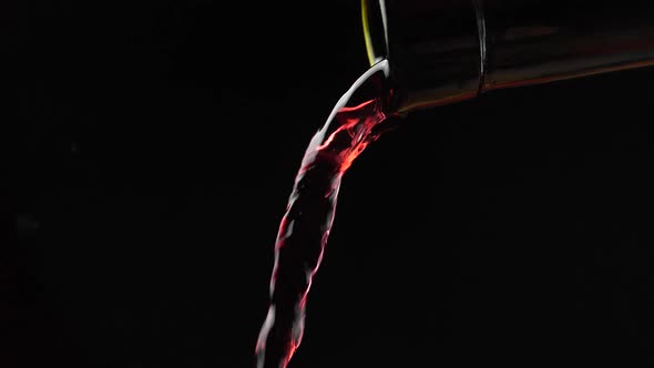 Wine. Red wine pouring from neck of bottle in wine glass over dark background. Rose wine pouring fro