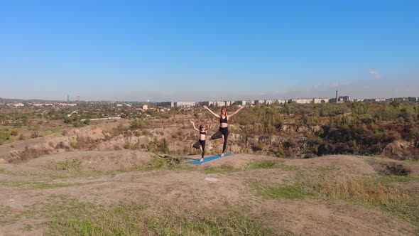 Aerial Drone View of Slender Young Mother Do Yoga Exercises with Child Daughter on High Hill By Lake