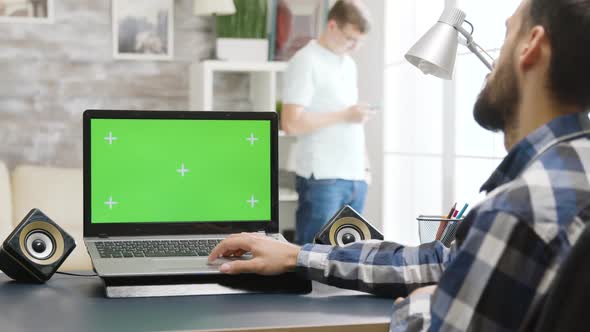 Over the Shoulder Parallax Shot of Man Working on Laptop with Green Screen
