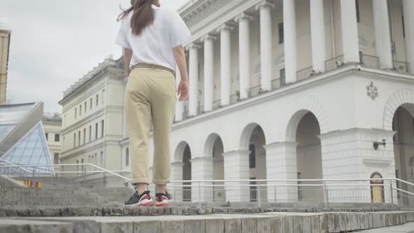 Young Cheerful Girl in Headphones Walking Up Urban Stairs and Dancing Robot Dance. Portrait of