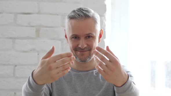 Inviting Middle Aged Man with Hands while Sitting in Office